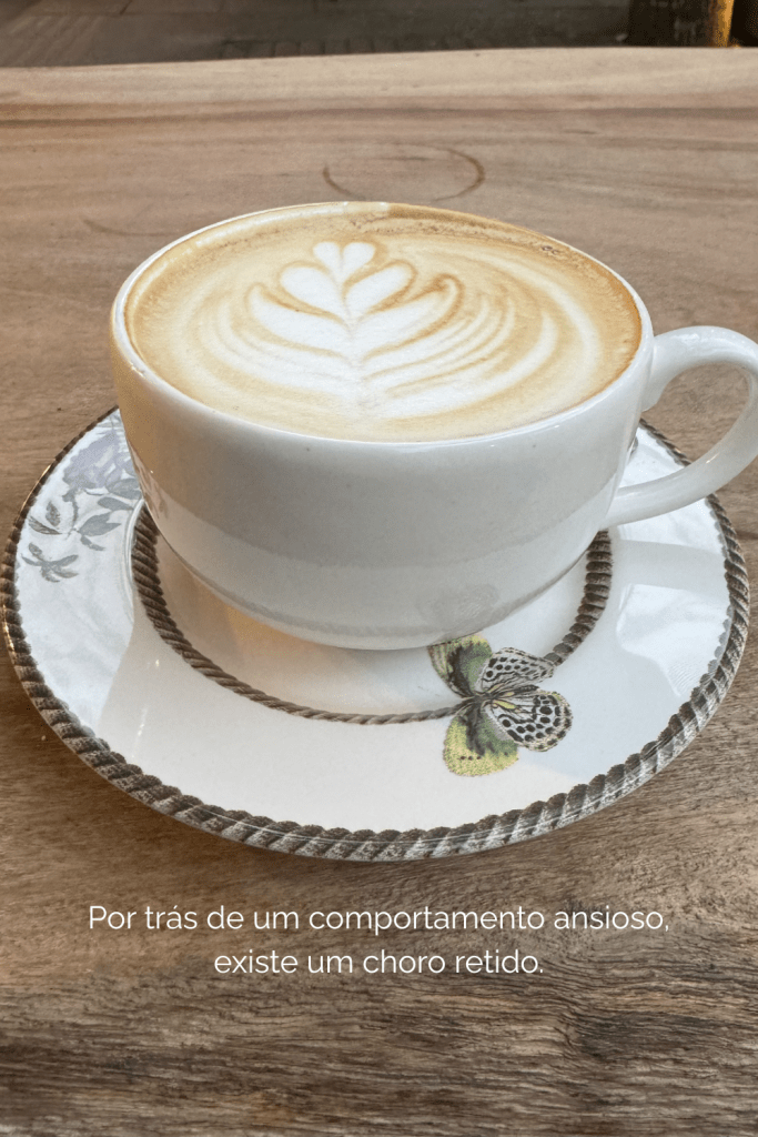 Uma xícara de café sobre uma mesa com o texto: Por trás de um comportamento ansioso, existe um choro retido.